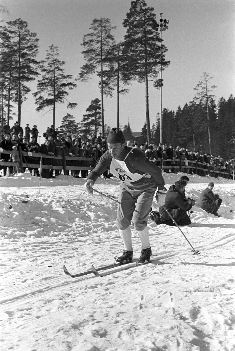 Skiløper med startnummer 83 i Holmenkollen. Publikum langs løypa.  Pressefotografer på sidelinjen. Holmenkollrennene 1963.