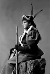 Portrett, kvinne sitter med skistav i hånda og ski mot skuld