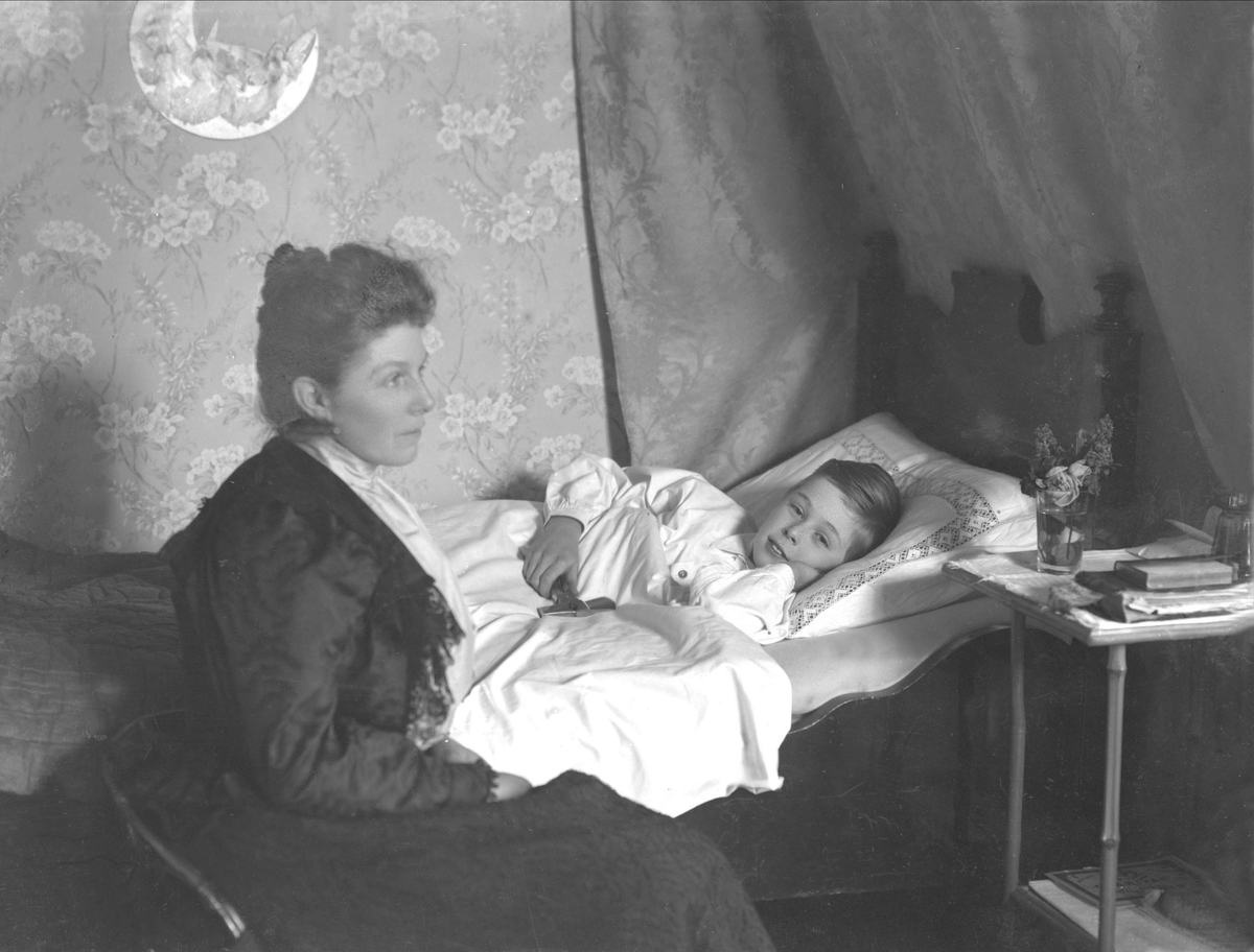 Interiørbilde, fru kammerherre Ekeberg sittende ved barnesengen. Et barn ligger i sengen.