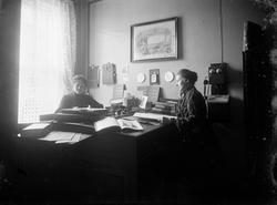 Kontorlokale, to kontordamer ved skrivebordet. Kjøpmann gala