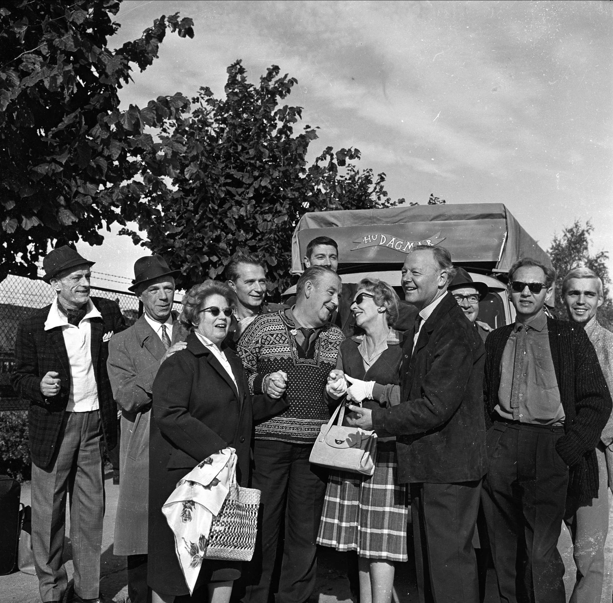 Alf Prøysen sammen med en gruppe mennesker, foran en buss med reklame for skuespillet "Hu Dagmar". NKL befaring, Oslo, 02.09.1964.