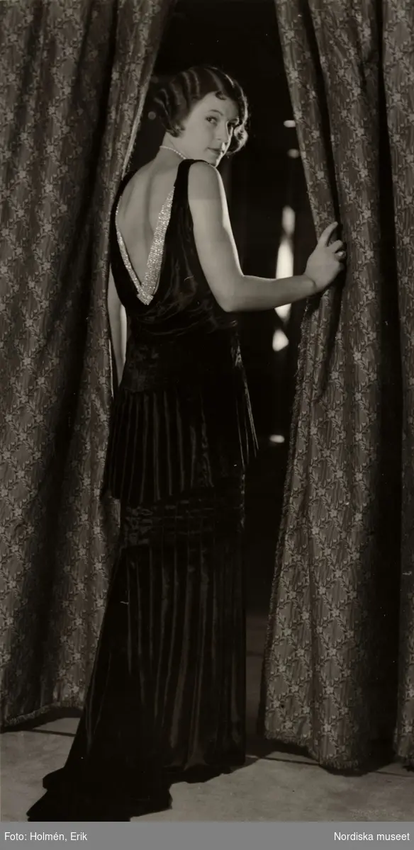 Nordiska Kompaniet, dammode. Kvinna vid draperi, iförd elegant aftonklänning med släp. NK:s franska damskrädderi den 19 mars 1930.