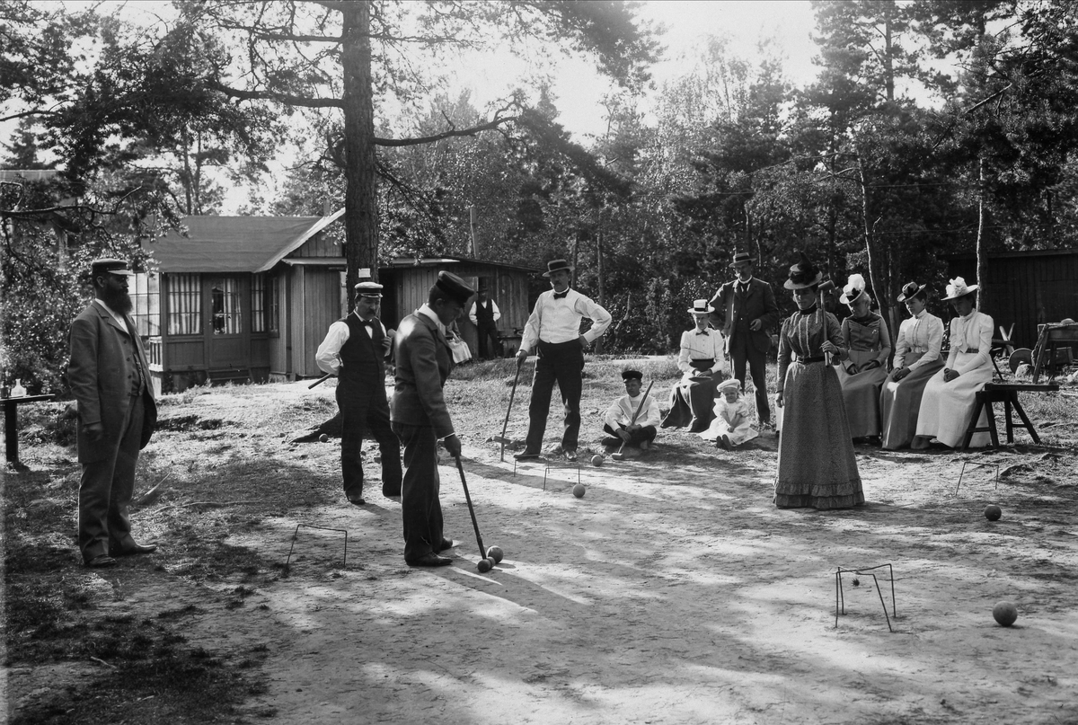 Män och kvinnor spelar krocket framför hus på Lidingö. 