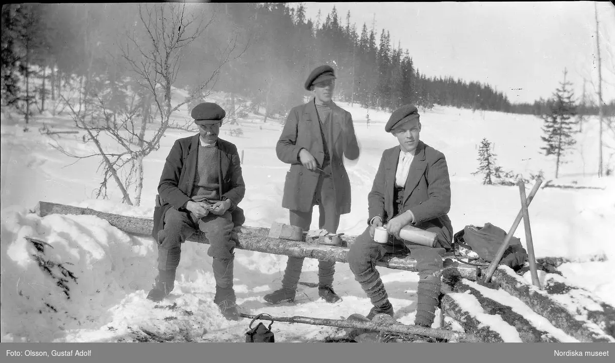 Tre män har matpaus ute på vintern. 1900-talets första hälft.