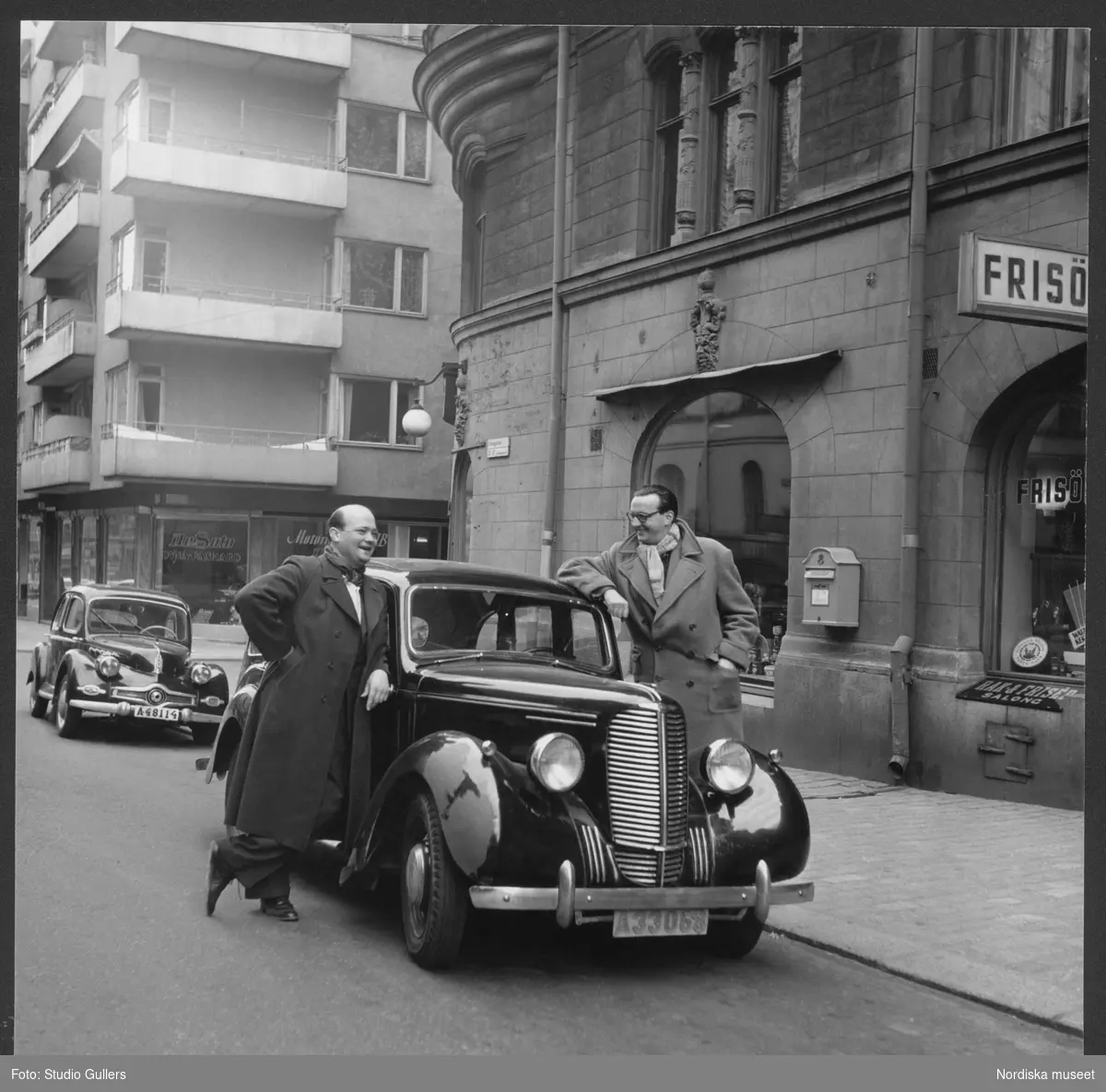 Författaren Stieg Trenter och fotografen KW Gullers vid en bil av modell Hillman Minx. Parkerad i bakgunden en Panhard Dyna X. Linnégatan, Stockholm.