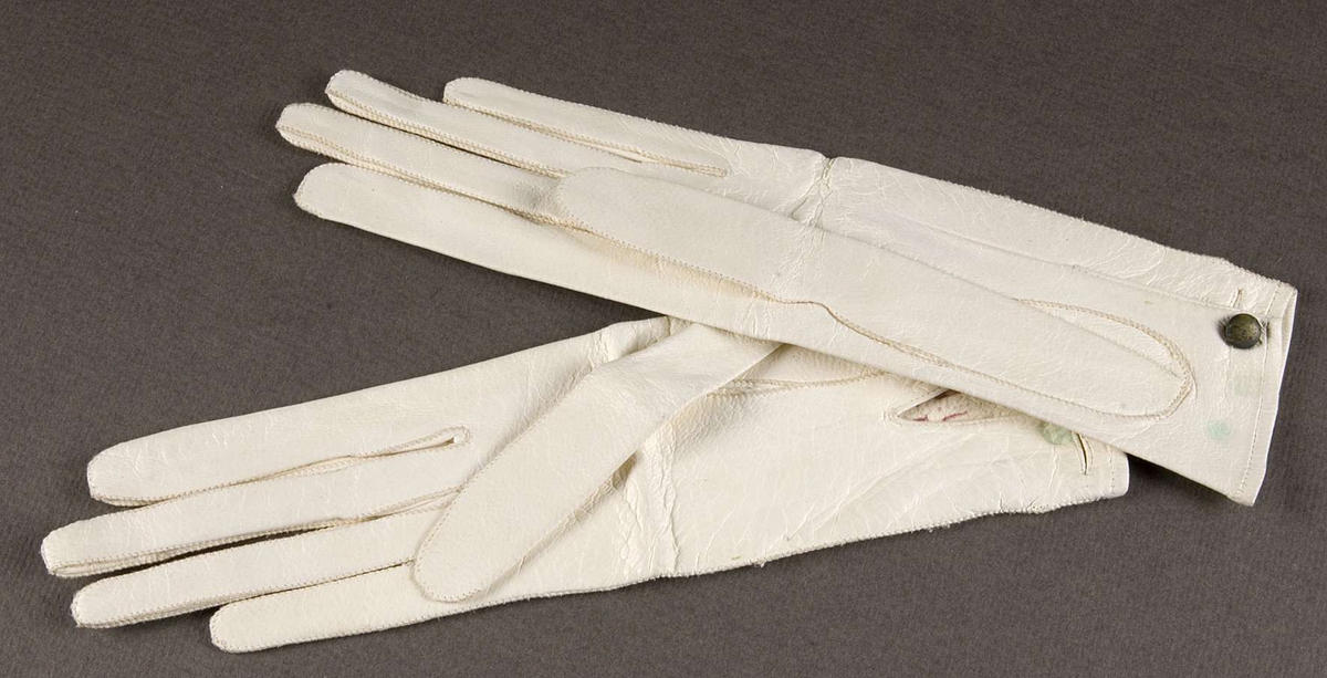 Ett par handskar av vitt glaceskinn, ofodrade, sydda med kastsöm. Knäppta med liten mässingsknapp. Stämplade med rött: F. Krook Silvermedalj 1860 Göteborg 6 ½.