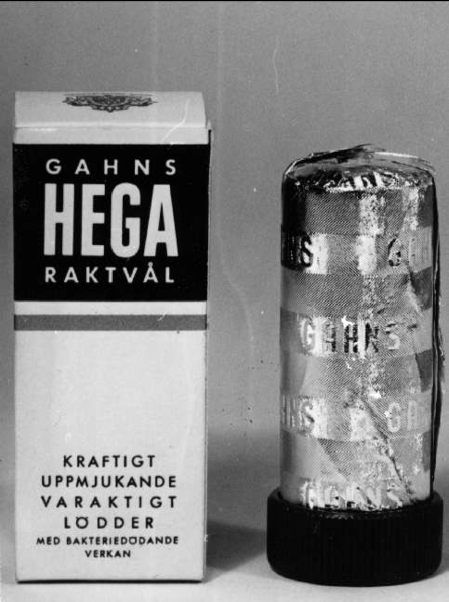 Ask med raktvål av märket Hega. Tillverkare: Henrik Gahns aktiebolag, Uppsala. Tvålen sitter i en grön trähållare. På asken står "Kraftigt uppmjukande, varaktigt lödder, med bakteriedödande verkan".