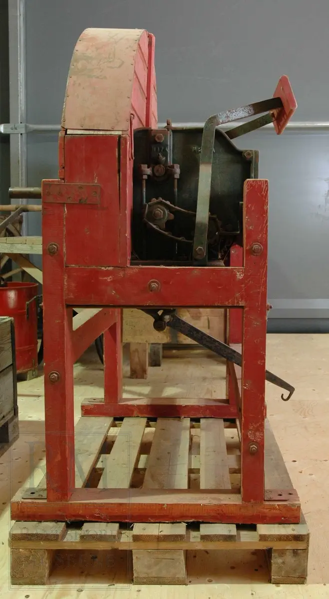 Rødmalt hakkelsmaskin i tre med tannhjul og kniver i jern. Svinghjulet mangler. 