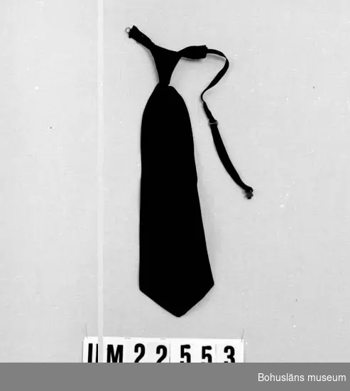594 Landskap BOHUSLÄN

Färdigknuten svart slips. Resårband med hake och hyska. 
Fastsydd rund liten papperslapp med text: "M 2:-."

UMFF 120:5