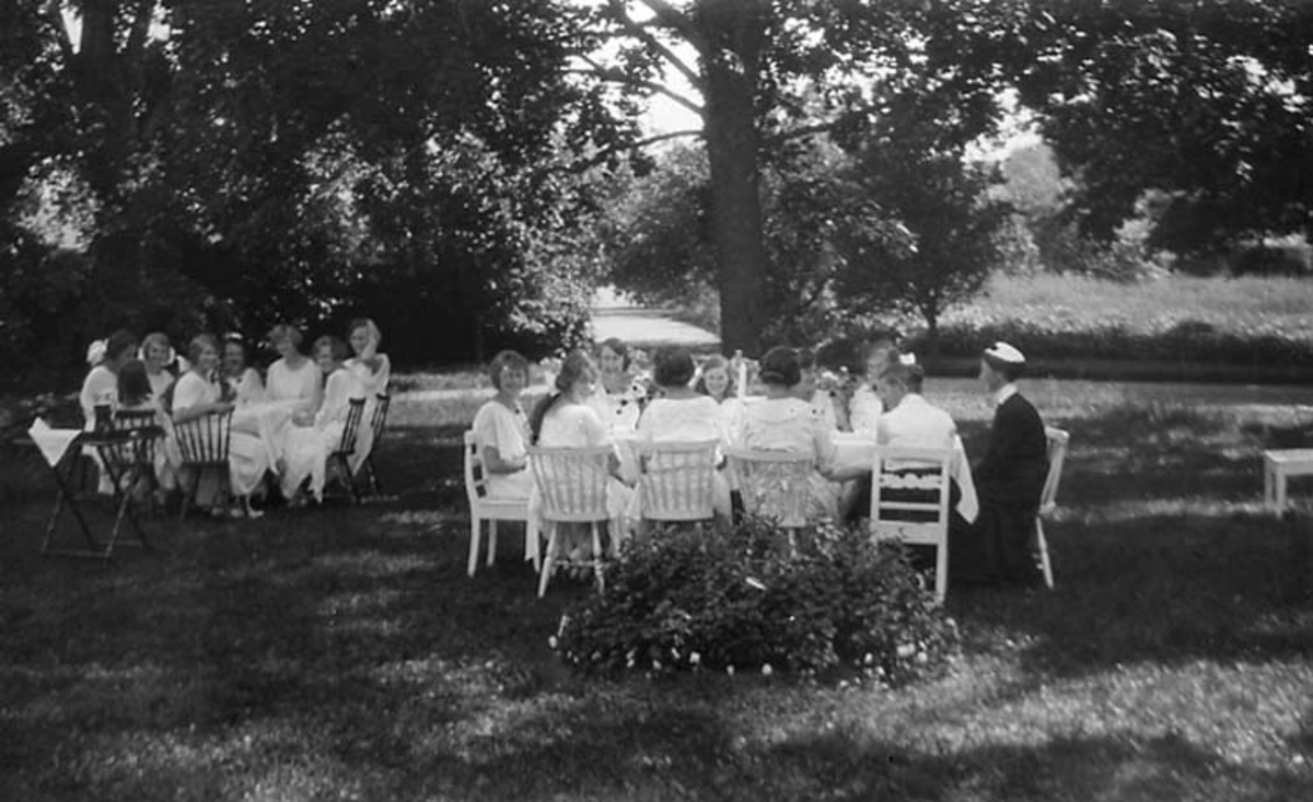 Dukade bord under trädens grönska. Unga kvinnor har samlats vid två bord.