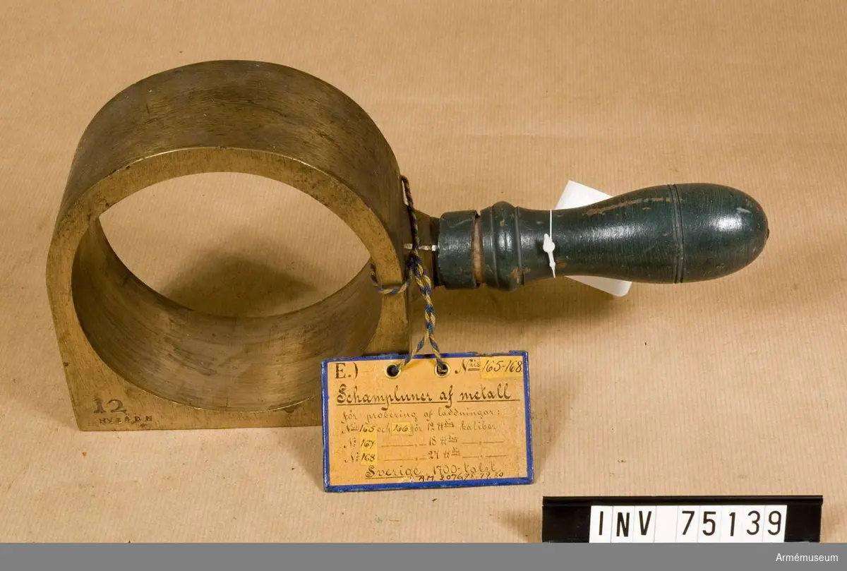 Grupp F:III(överstruket) V. 
Schamplun av metall med handtag av trä för prövning av färdiga karduser eller skott av 12-pundig kaliber. 
