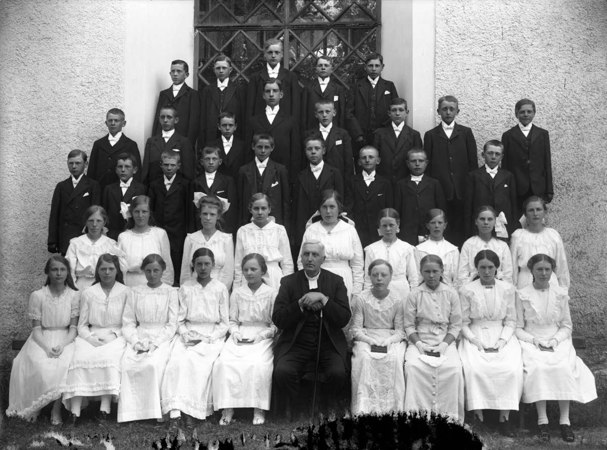 Konfirmandgrupp vid Simtuna kyrka, Uppland, troligen 2 juli 1917.  I mitten kyrkoherde August Hylander (1852-1935).