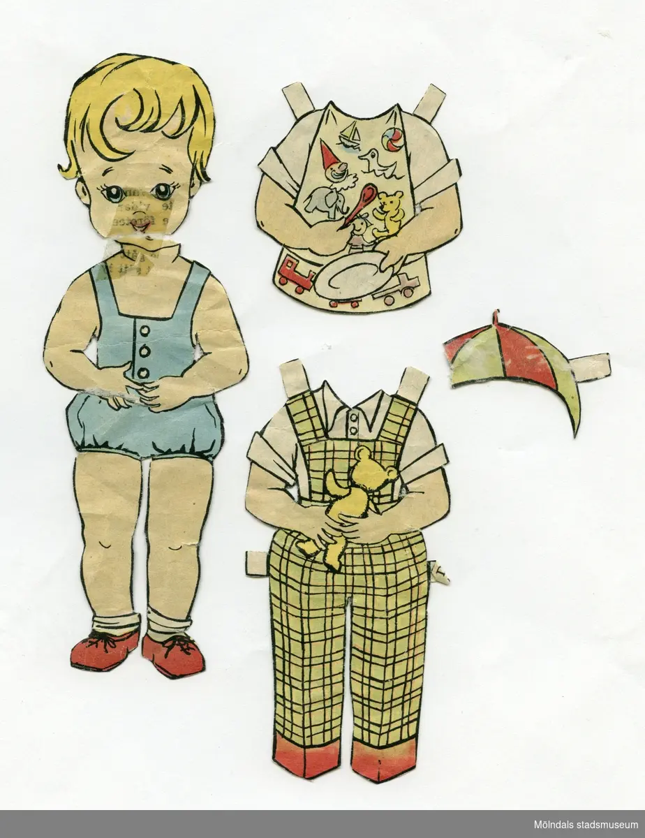 Klippdocka med kläder, urklippt ur tidning på 1950-talet. Docka och kläder märkta "Lasse" på baksidan - dockans namn. Dockan föreställer en liten pojke, med blont hår, iklädd lekdräkt med korta ben, strumpor och skor.Garderoben består av hängselbyxor med skjorta, skjorta med hakklapp, tallrik och sked, samt mössa (saknas en bit). 