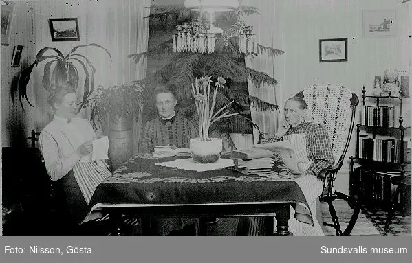 Tre kvinnor som sitter vid ett bord med böcker. Anteckning "Fr. Söderberg"