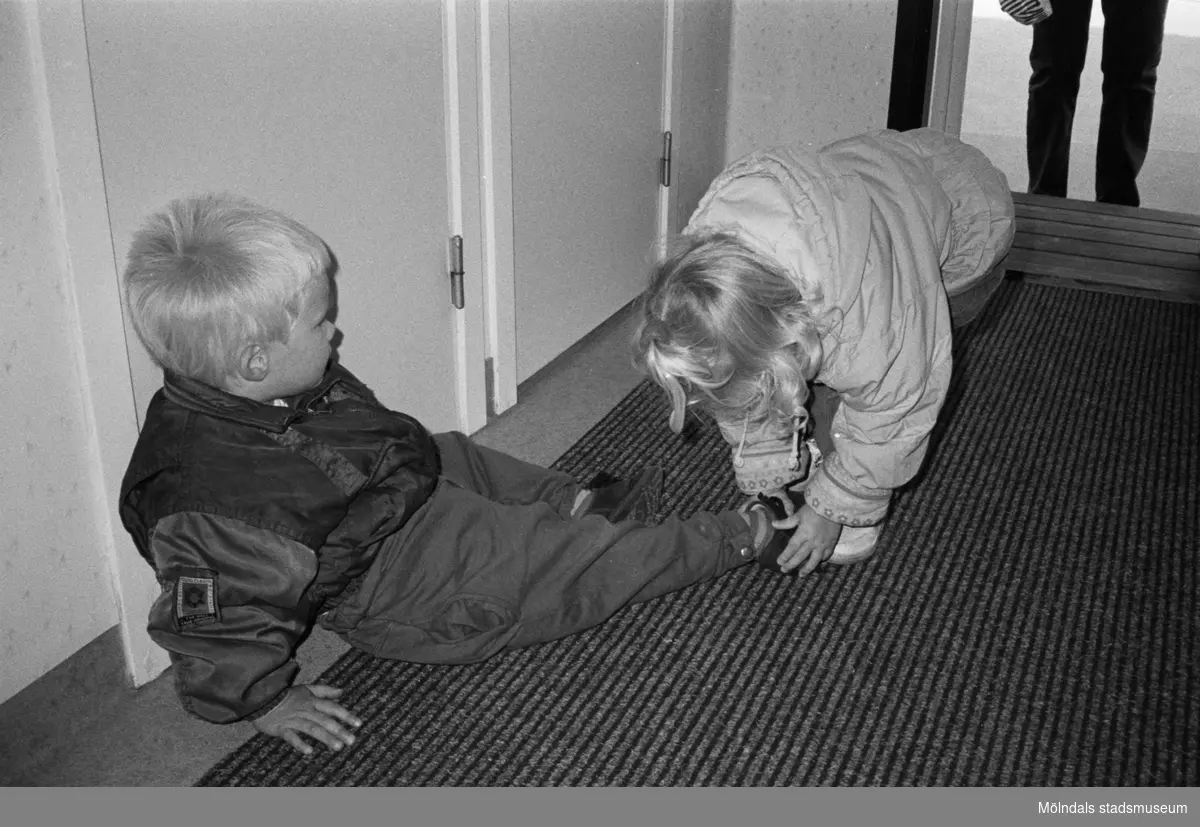 Robin, som sitter på innegolvet, får hjälp med sina skor av ett annat dagisbarn. Hoppetossan, Katrinebergs daghem, 1992.