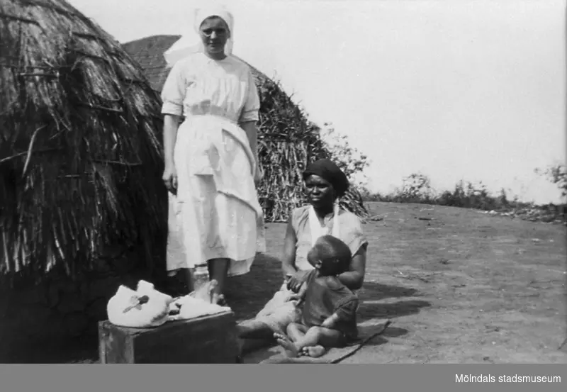 Helga Andréasson (f. 12 nov. 1904) står bredvid några bybor i Sydafrika, omkring 1931.
Helga var diakonissa samt sjuksköterska. Var anställd av Svenska Kyrkans missionsstyrelse från 1 april 1931 till pensioneringen 30 nov. 1969. Hon verkade under denna tid som missionär i Sydafrika där hon tjänstgjorde som sjuksköterska vid olika sjukhus.