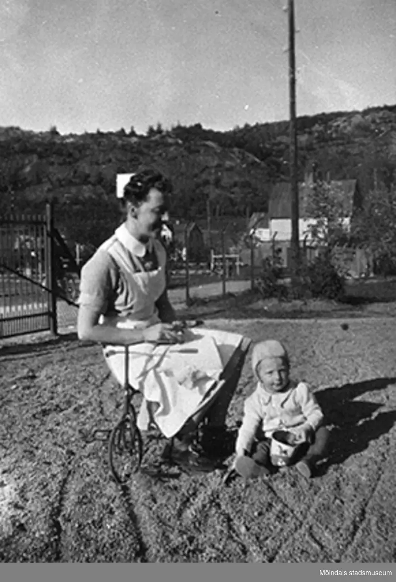 En lärare som sitter på en trehjuling och ett litet barn som sitter bredvid, Krokslätts daghem, Dalhemsgatan 7 i Krokslätt. 
Under Margit Emilssons (gift Wannerberg -52) praktik som biträde
1945-10-01 - 1946-08-01.