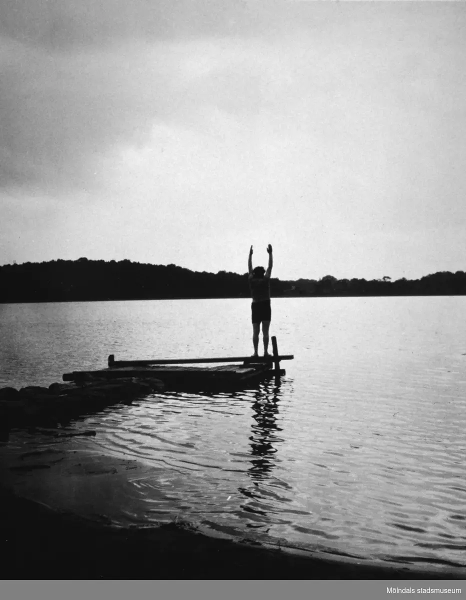 En person står med uppsträckta händer längst ut på en brygga, troligtvis vid Tulebosjön cirka 1930.