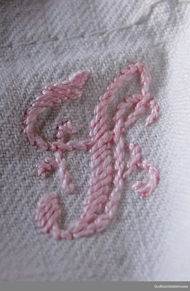 Fire hvite laken med brodert bokstav i rosa i ene hjørnet.