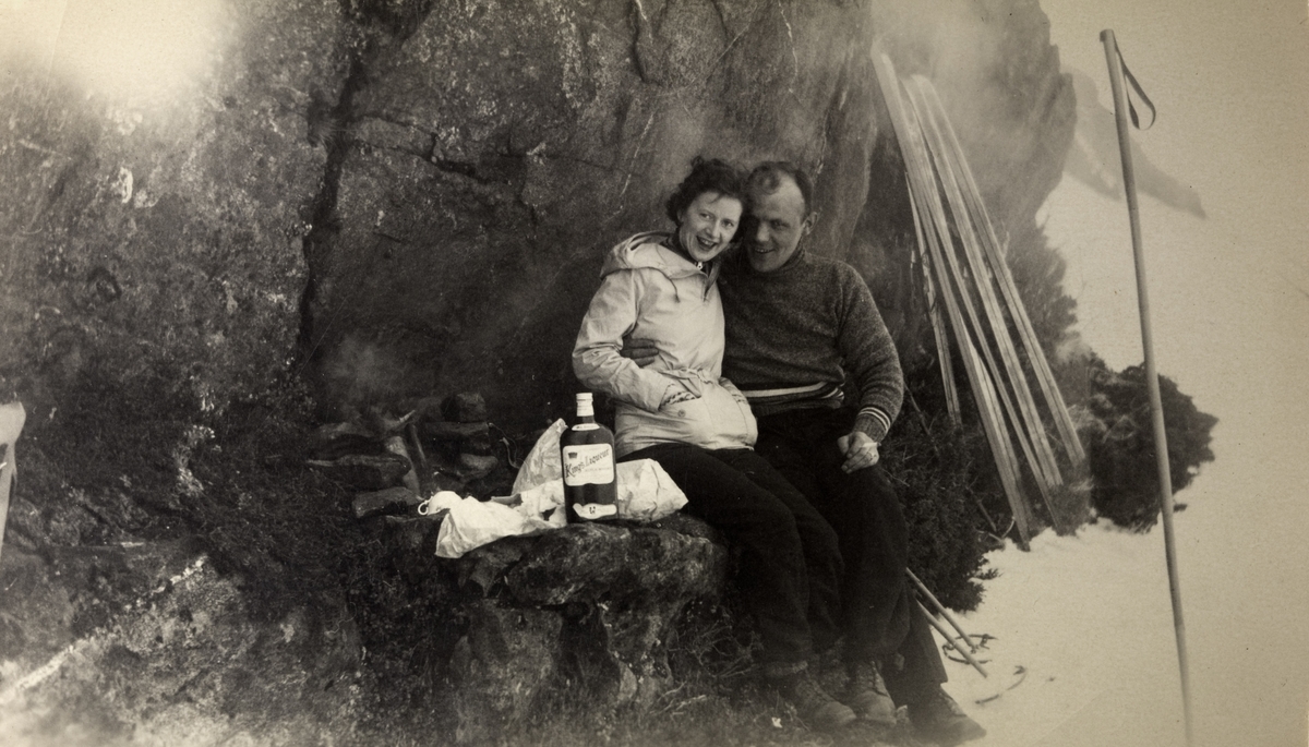 Kvinne og mann tar pause under en skitur, og koser seg med en medbragt flaske whisky.