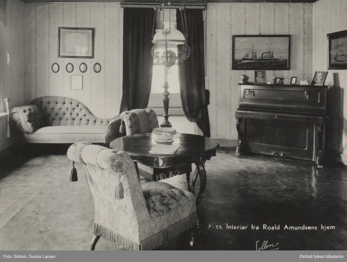 Interiør fra stuen, til "Tomta", Vesten i Borge, Roald Amundsens fødested. Sofa, stol og bord, lampe og piano. Hjemmet til skipsreder Jens og Olga Amundsen. Postkort.
