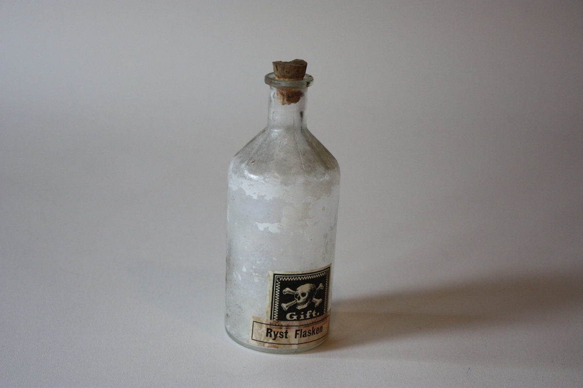 Rund flaske med kork. Har innehalde væske med kvitt tørrstoff. Merkt med giftmerke og stempel Gift Ryst flasken.
Sjå SUM.10888.