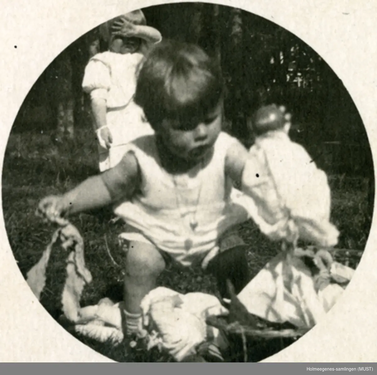 To barn leker utendørs. Sirkulært foto kopiert på postkort-papir. Postkortet er påskrevet og poststemplet Wien august 1922.