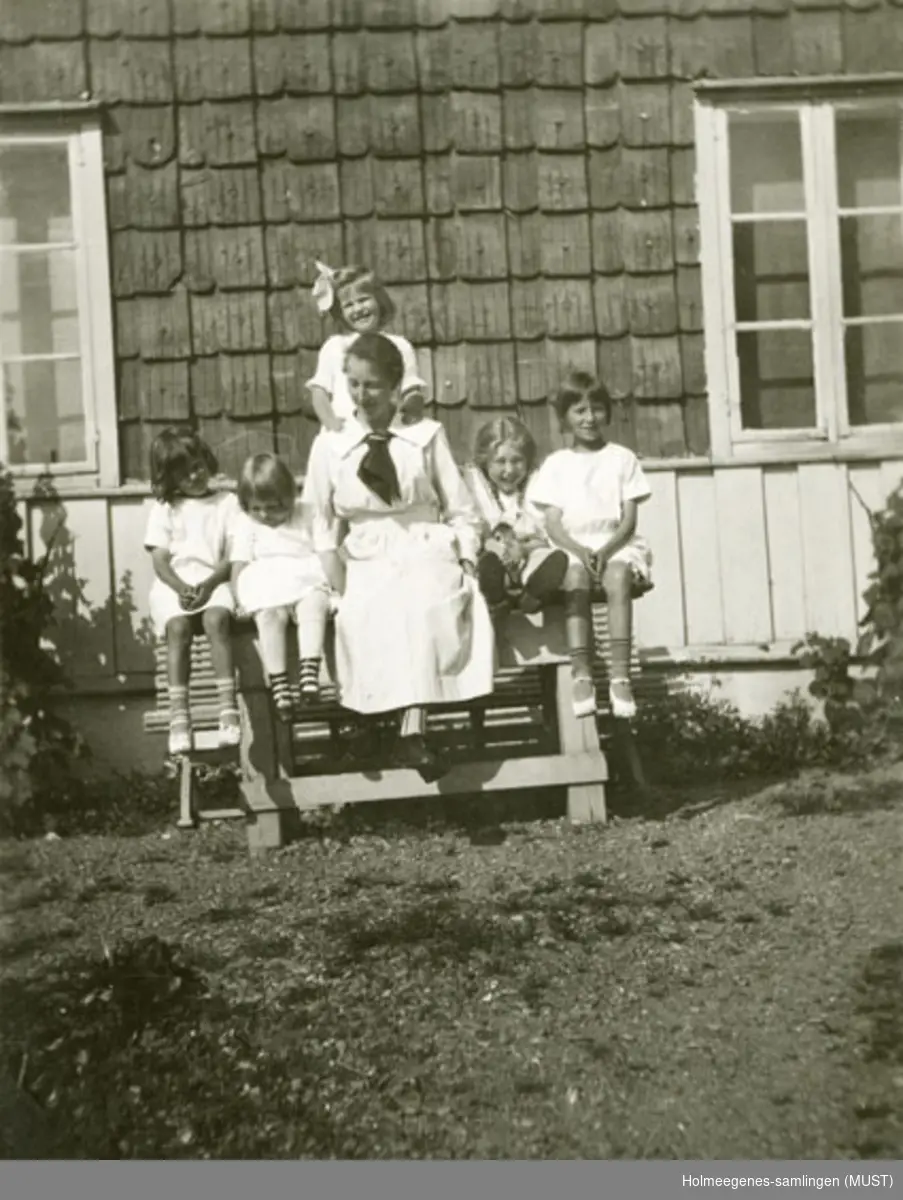 Foran huset på Holmeegenes i Stavanger. En kvinne og fem jenter sitter på et hagebord.