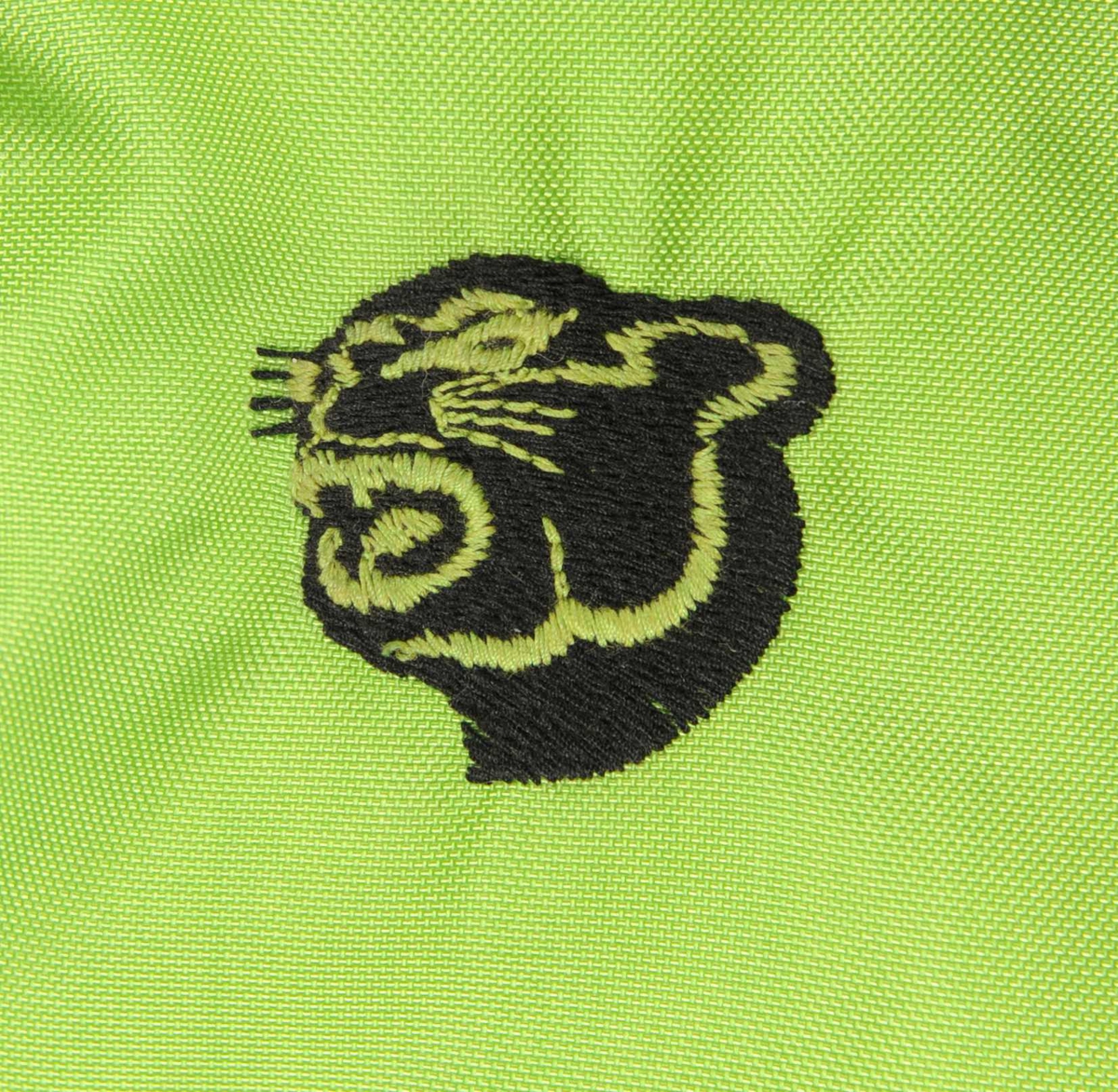Dress av syntetisk stoff i fargene grønt, svart og hvitt. Halsen og enden på ermene er av et strikket stoff. Dressen lukkes ved hjelp av en glidelås og et belte. Det er to lommer. Det er et tekstilmerke med brodert kattehode på venstre siden under skulderen.