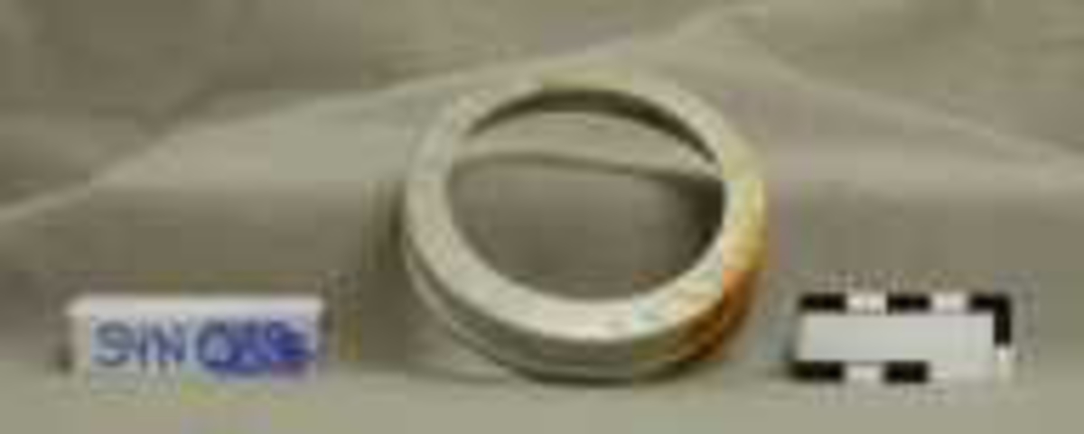 Del 1 er en ring i metall, med riller langs kanten, i ringens høyde. Ringen har skrufeste innvendig. 
Del 2 er en skive i støpt, gjennomsiktig glass, med innskrift på toppen. 