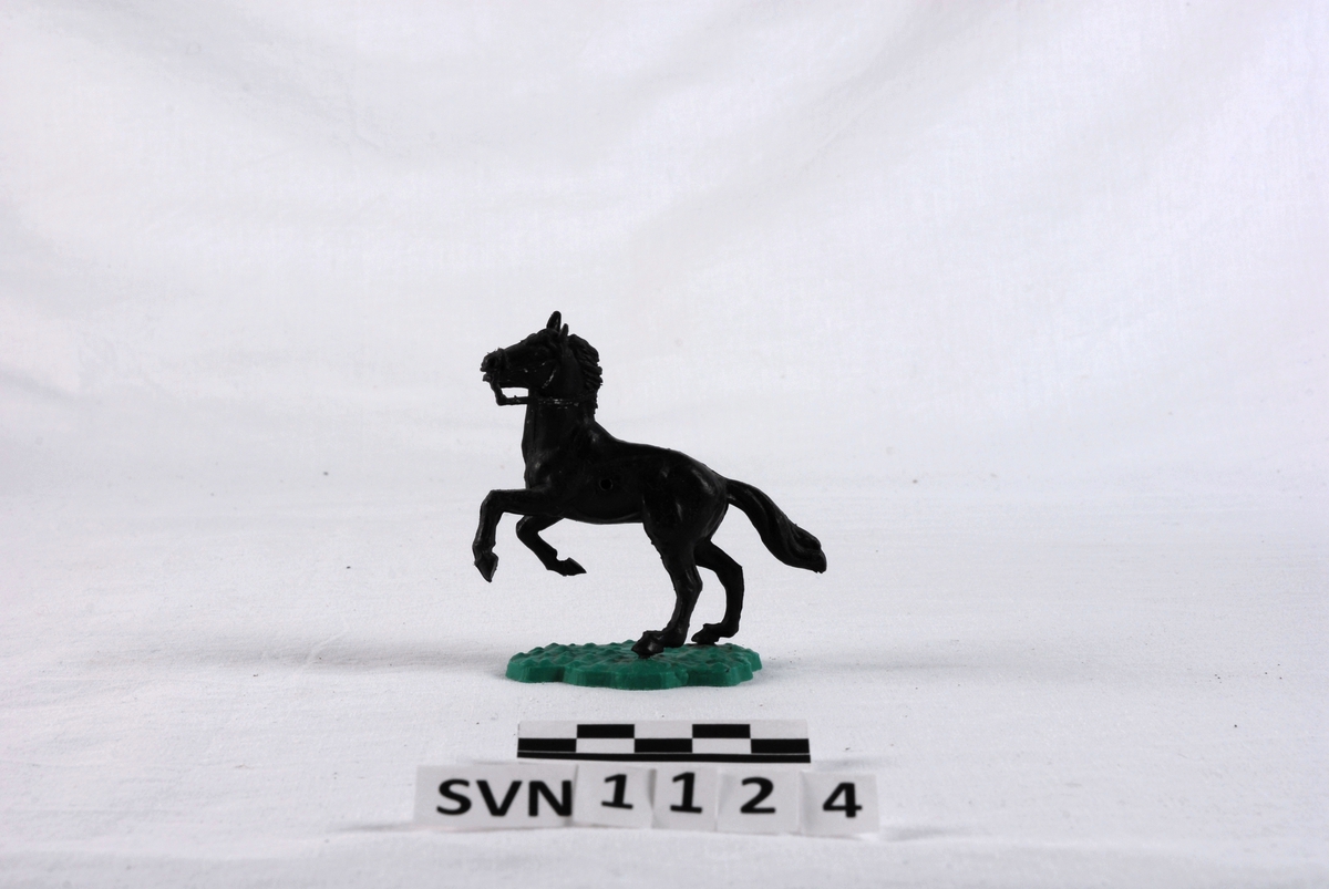 Liten plastfigur. En svart hest som står på et grønt underlag