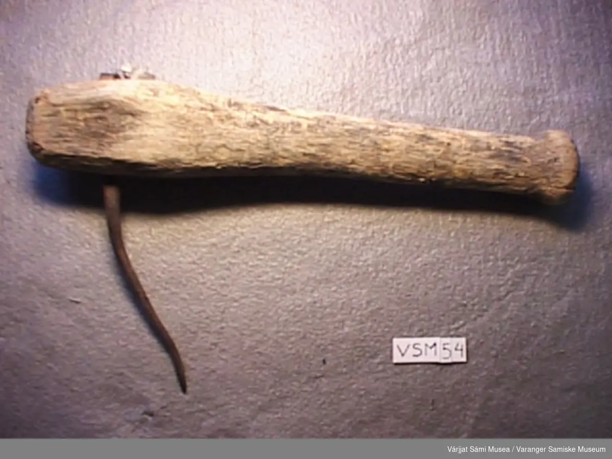 En klepp, håndtak av tre med krok av jern. Den er ca. 40 cm lang, mens jernet er ca. 10 cm langt.