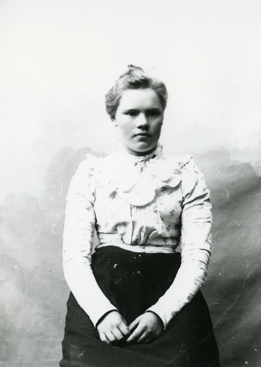 Kvinne kledd i lys mønstrete bluse, i halvfigur, med lerretbakgrunn