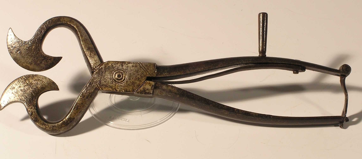Form: saks med store økseblader som møtes; fjæranordning og lås; rund pigg på en av armene til saksen

