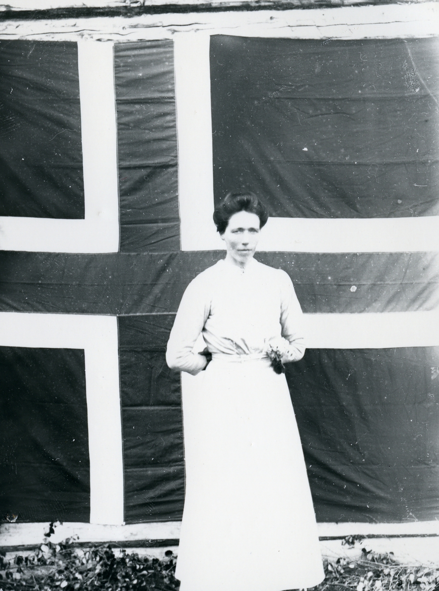 Kvinne i helfigur, stående foran norsk flagg som lerret