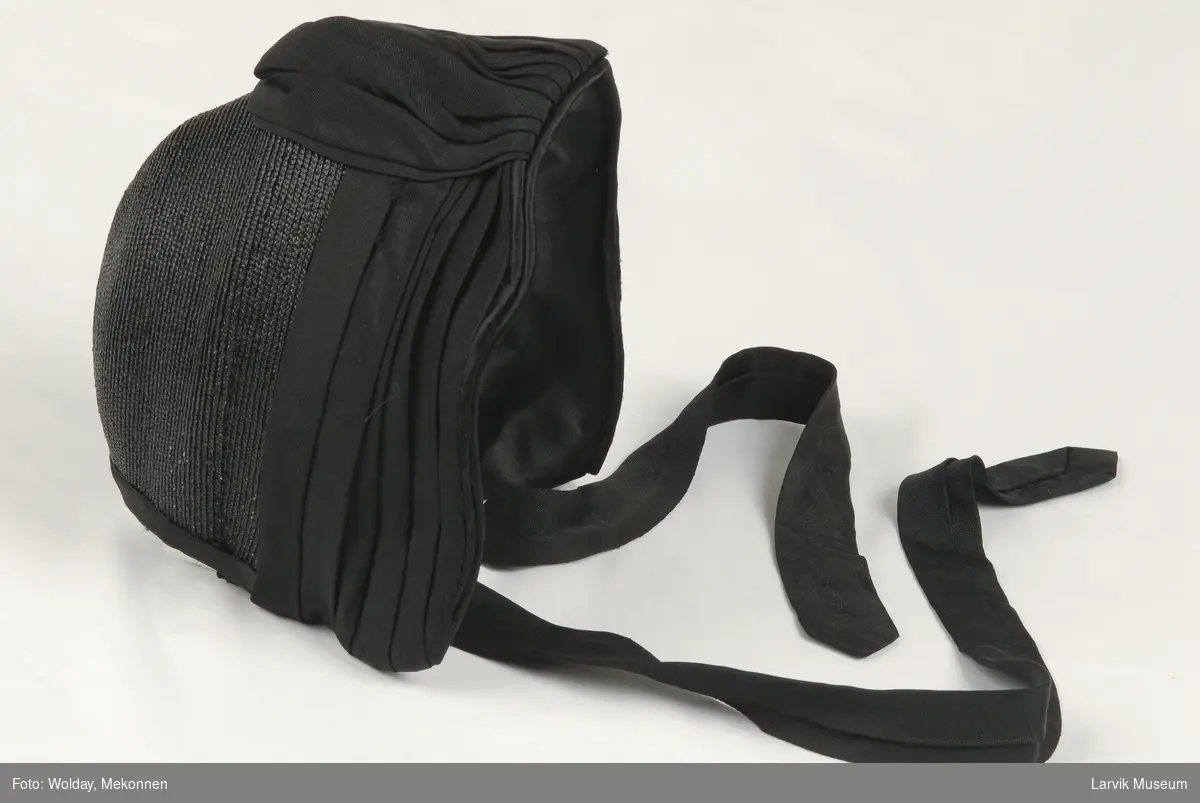 Form: liten kyse fasong, Besetning i forkant med draperi midt foran av sort krypert silkestoff noen går over i knytebånd.

