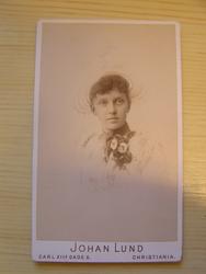 Dame med hatt, pynt på kjole ved hals.