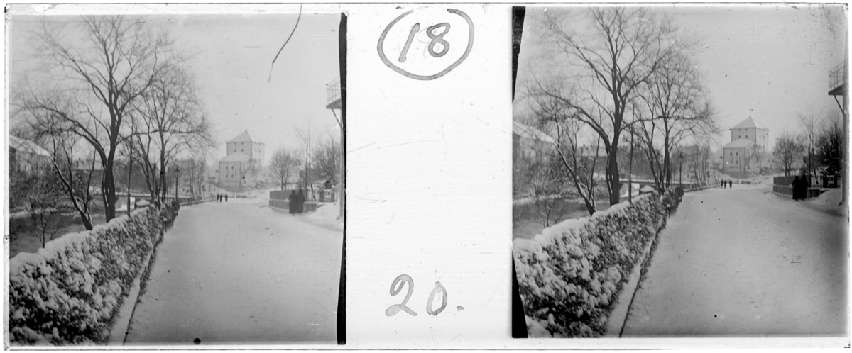 'Bildtext: ''Strömgatan, nedåt.'' :: Gatuvy med snöklädd mark, människor promenerar på vägen, vy med häck längs gatan. På avstånd byggnader, hus och bro över ån. ::  :: Ingår i serie med fotonr. 5256:1-18, se även hela serien med fotonr. 5237-5267.'