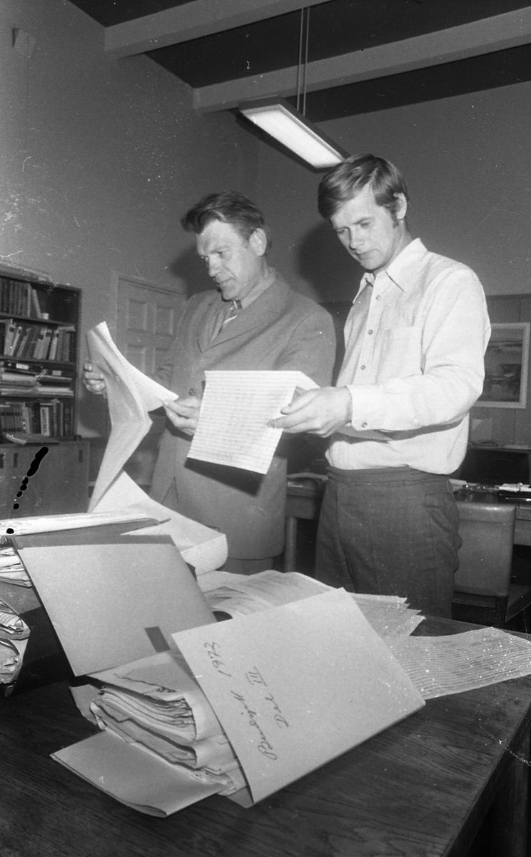 To menn som studerer diverse sakspapirer.