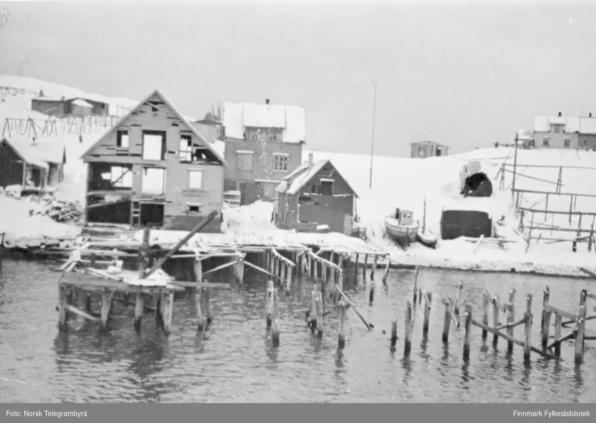 'I fiskeværet Båtsfjord i Vardø herred, som er en av Finnmarks beste naturlige havner, var ikke alle hus totalskadet, men bryggene var borte, og stedet har stygge sår etter krigen.' Bildet viser ødelagte kaier.