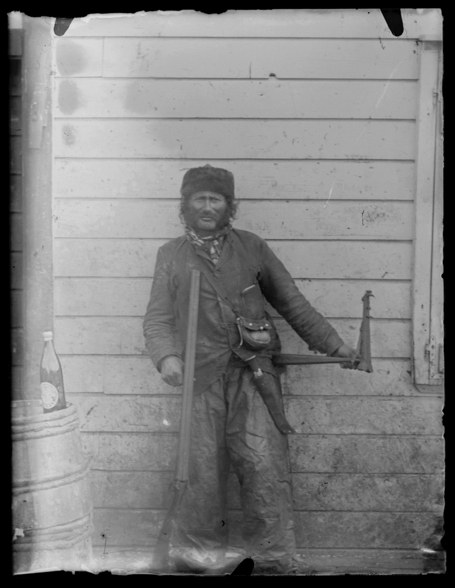 Mann med gevær foran en husvegg
