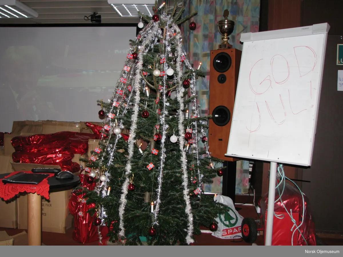 Ferdig pyntet juletre i kinosalen på plattformen. Ved siden av står det "GOD JUL" på ei tavle. I bakgrunnen ligger en stor mengde gaver.