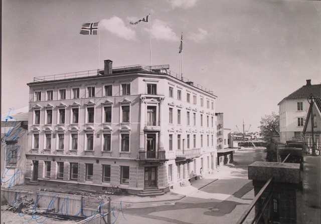 Bygate med hotellbygning i historisme. Fire -etasjes murbygning tv. med tre flaggstenger på taket. 1930 årene. Arendal, hotell Phønix.