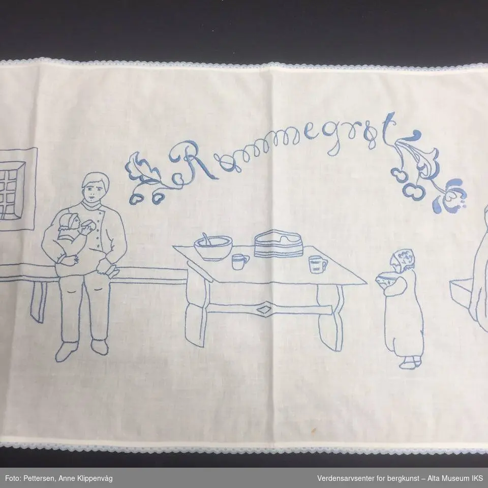 Rektangulært, hvit bordløper. Brodert motiv med blå tråd: Kjøkkeninteriør med tre personer.