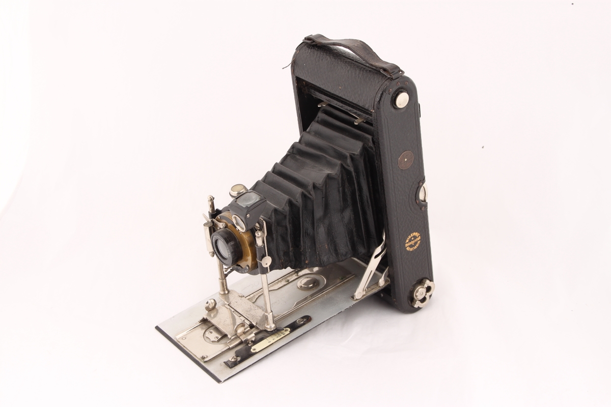 Et svart foldingkamera med utfellbart objektiv. Objektivet ligger trygt beskyttet inne i kameraet når det er sammenslått. På baksiden av kameraet er det en skyvbar veggplate som gir tilgang til kameraets innside.