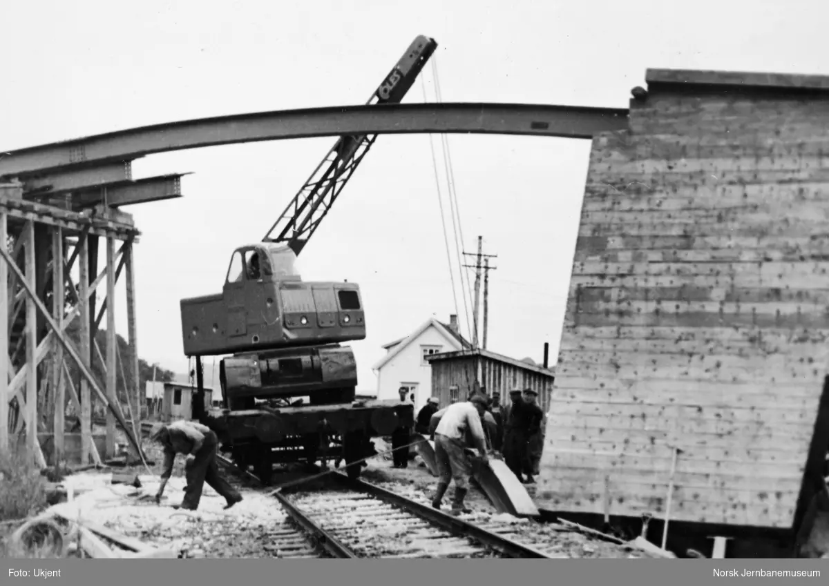 Anlegget Mosjøen-Mo i Rana : bygging av bruovergang ved Halsøy, pel 200, Havnevesenets kranbil opplastet på jernbanevogn