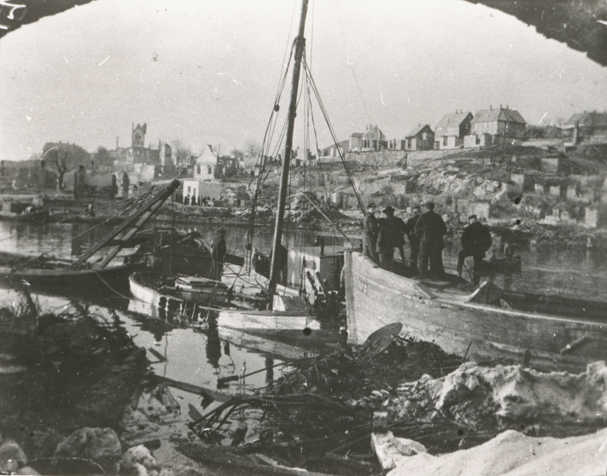 Menn samlet rundt forliste båter ved Aspøy etter bybrannen i Ålesund 1904.
