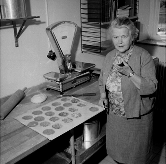 Konsum Bageriet, interiör, en kvinna.
Författaren Margit Palmer-Waldén med "Kajsa Warg kakor".