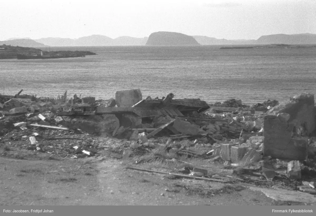 Ruiner av Hauans materialhandel. Foran på bildet er Nedre Grønnevoldsgate. Oppe til venstre på bildet ses Hammerfest-neset. En ganske stor fraktebåt ligger fortøyd rett foran neset. Øya Håja med Sørøya noe diffust ses øverst på bildet. Fuglenesodden ses oppe til høyre.