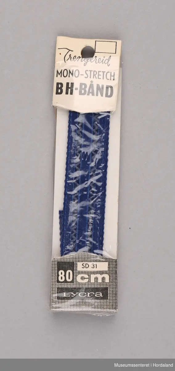 Mørkeblått BH-bånd i lycra, pakka i plast- og pappemballasje. Produsert av Trengereid Fabrikker: "nytt mykt elastisk BH-bånd som ikke ruller, glir eller strammer".